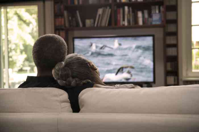 Una pareja ve la televisión escuchando el sonido con audífonos retroauriculares