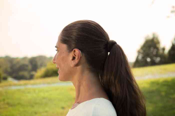 Perfil de una mujer con audífono retroauricular en un parque