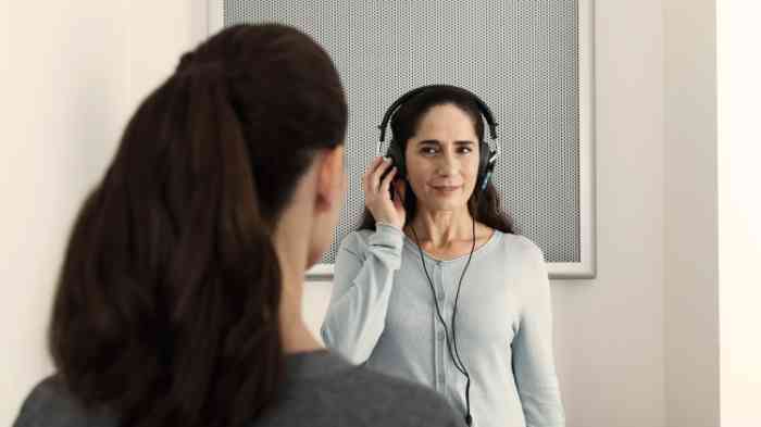 Una mujer escucha el sonido de su móvil con un audífono retroauricular