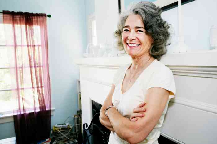 Una mujer mayor de pelo blanco sonríe en su casa