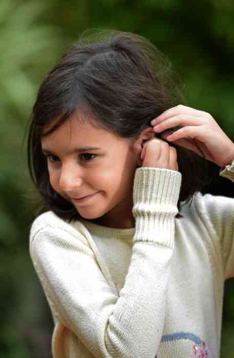 Una niña se pone un audífono en el oído